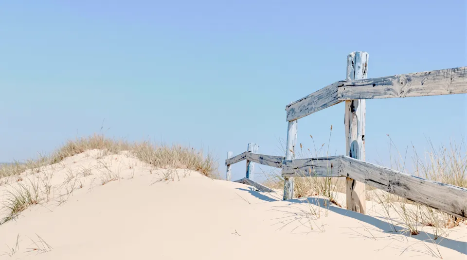 AI-generated illustration: sand dunes with a weathered wooden fence at midday