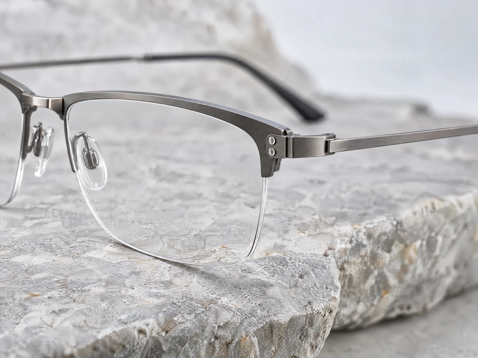 A semi-rimless titanium eyeglass frame in matte gunmetal on pale stone, close up