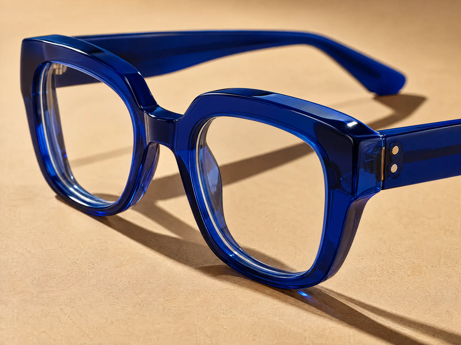 An oversized cobalt blue acetate eyeglass frame on a sand-coloured surface
