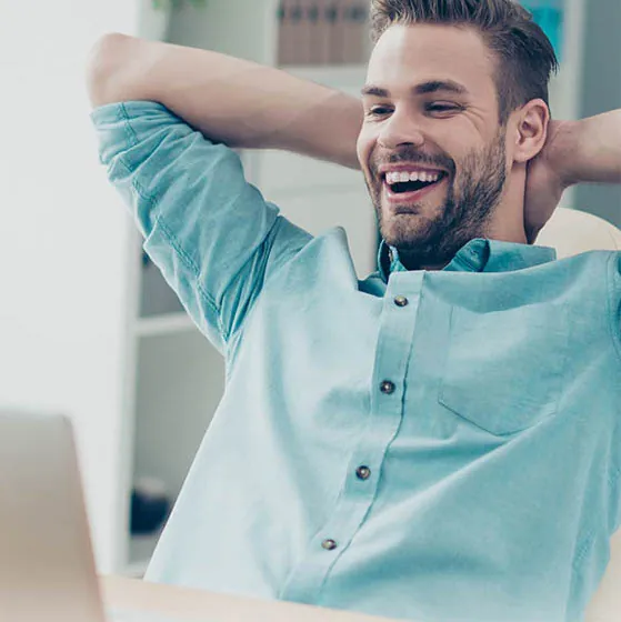 Smiling man leaning back in chair while looking at laptop