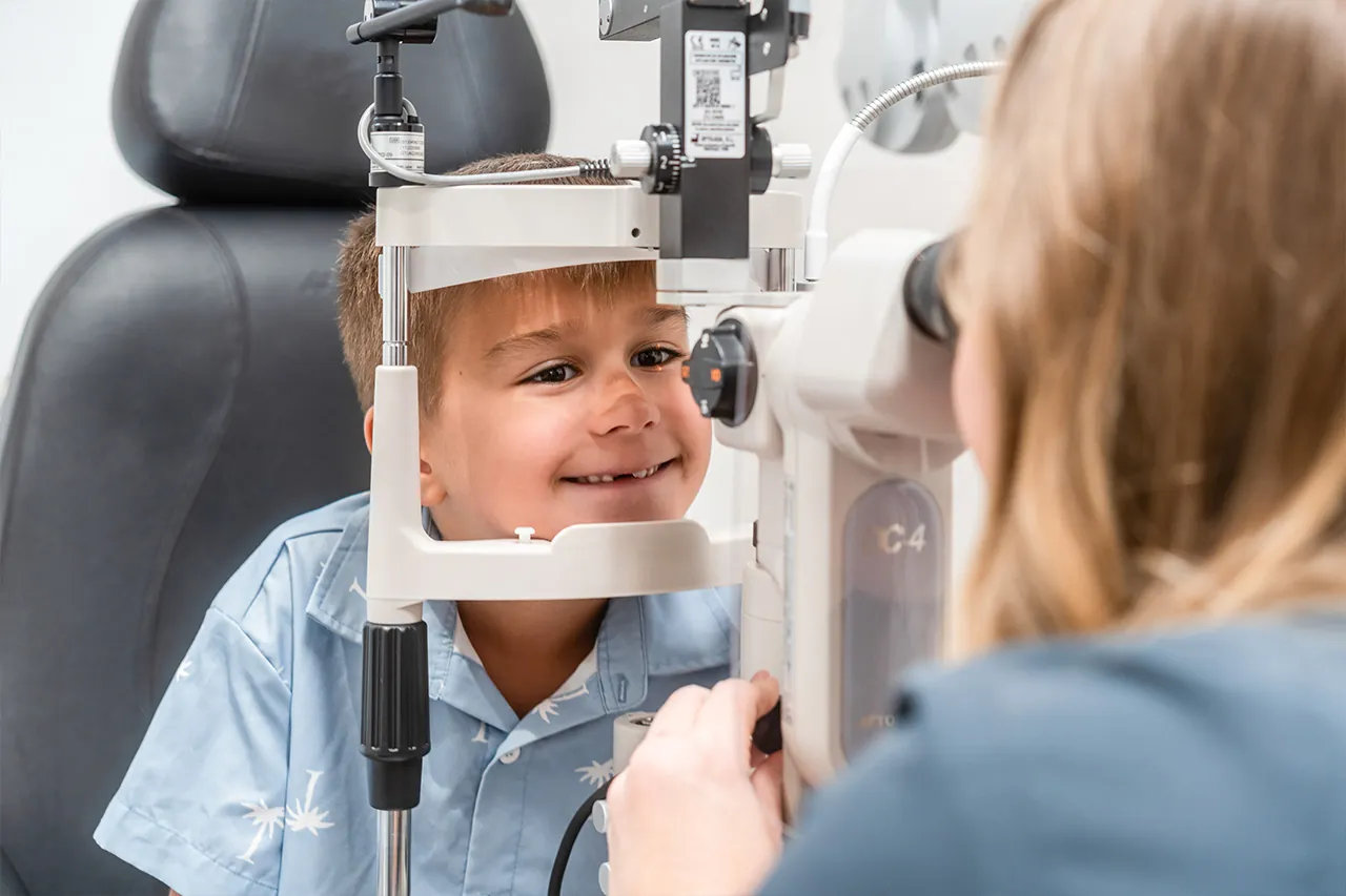 Young boy smiling during slit lamp eye exam at clinic