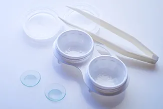 Contact lens case with tweezers and lenses on blue surface