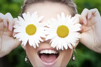 Smiling woman playfully holding daisies over her eyes