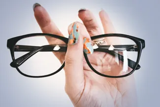 Hand holding black eyeglass frames against a light background