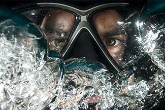 Man underwater wearing swim goggles with bubbles around face